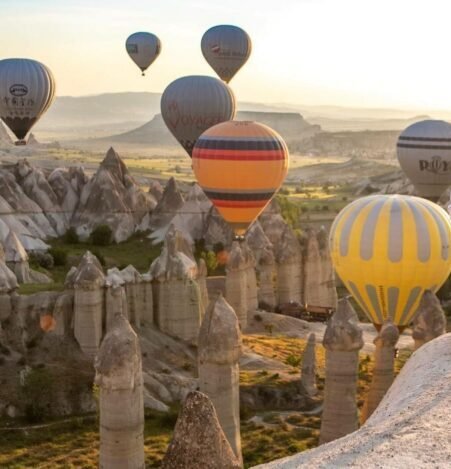 Sunrise hot air balloons floating over the fairy chimneys of Love Valley in Cappadocia, with two people standing in the foreground enjoying the panoramic view